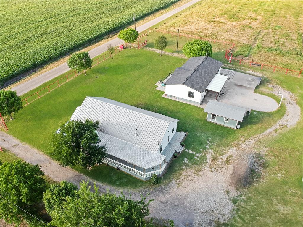 Expansive property featuring two structures with pitched roofs, a smaller auxiliary building, and a gravel driveway Expansive property featuring two structures with pitched roofs, a smaller auxiliary building, and a gravel driveway