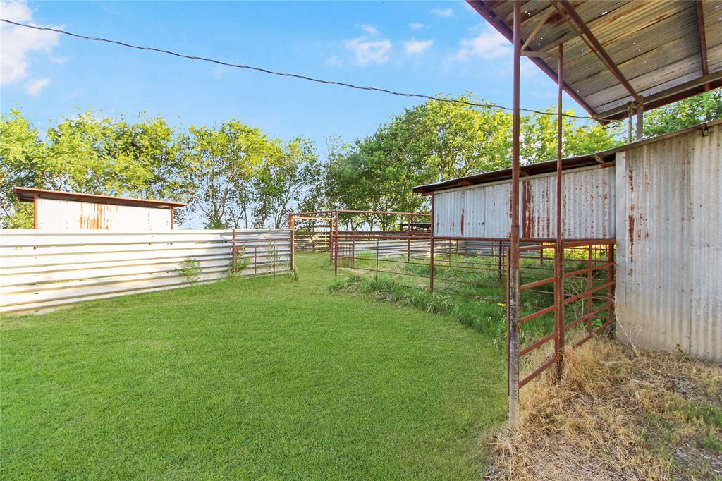 Outdoor fenced area featuring a grass lawn, corrugated metal fencing, and multiple metal corrals
