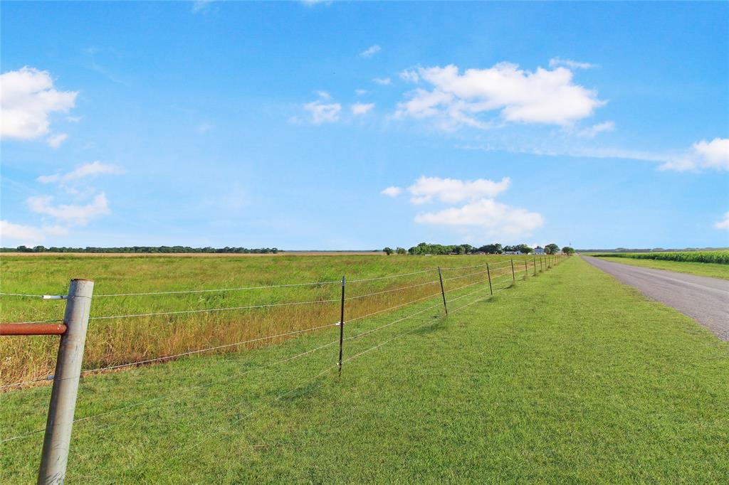 Expansive green fields alongside a paved road, bordered by a wire fence with metal posts