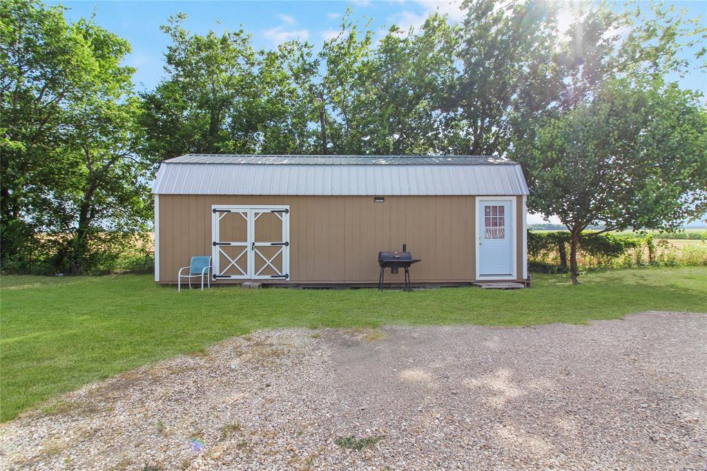 Freestanding outbuilding with a corrugated metal roof, tan siding, and white trim