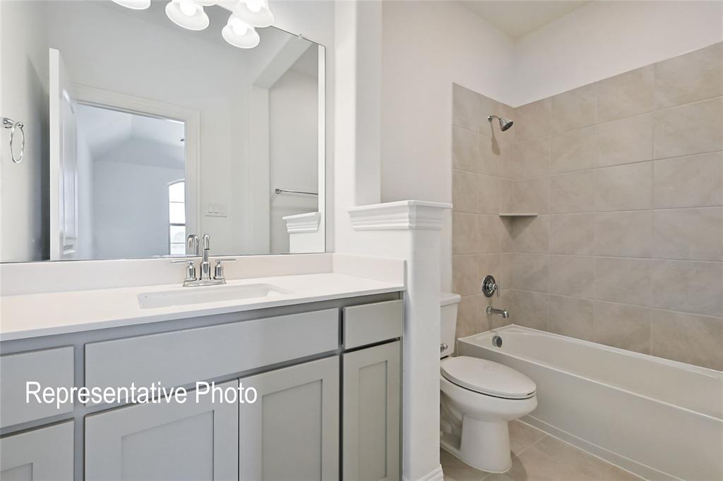Light-toned bathroom featuring a single vanity with a white countertop and chrome faucet, a large frameless mirror, and a bathtub with tile surround