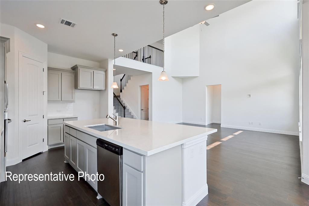Open-concept living space featuring a spacious kitchen island with integrated sink, stainless steel dishwasher, light gray cabinetry, and high ceilings