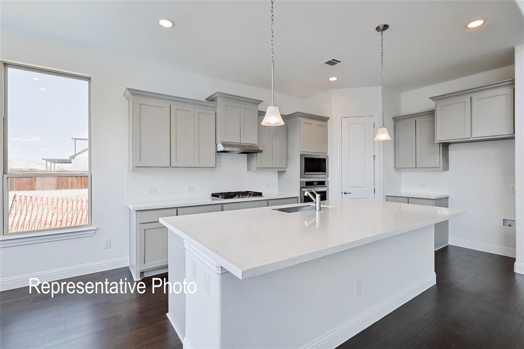 Spacious kitchen featuring an expansive island with a stainless steel sink, light gray cabinetry, white quartz countertops, white subway tile backsplash, and dark wood-finish flooring