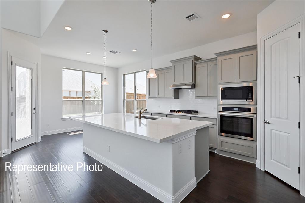 Kitchen featuring a large central island with a sink, light-colored countertops, and pendant lighting