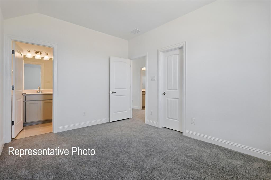 Carpeted room with a doorway revealing a bathroom featuring a vanity with a mirror and multi-bulb fixture