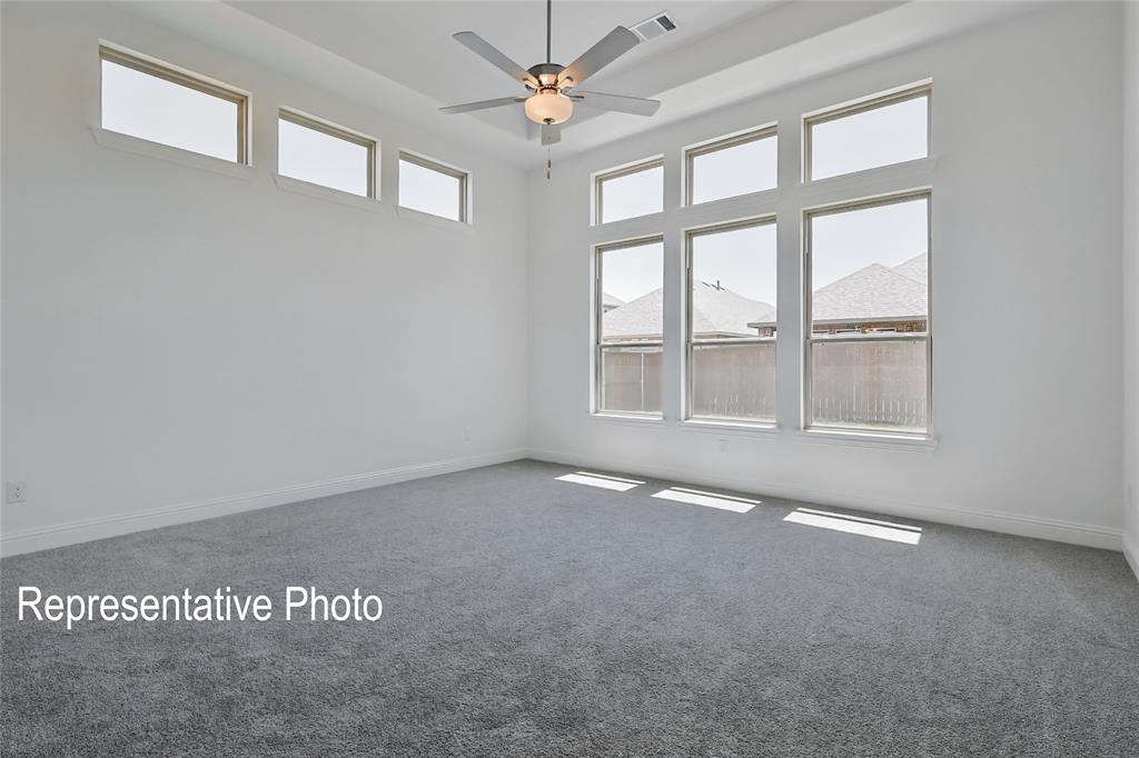 Spacious room featuring gray carpeting, white walls, multiple large windows, a ceiling fan with integrated lighting, and a high ceiling