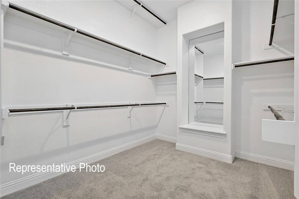 Spacious walk-in closet featuring extensive built-in shelving, multiple hanging rods, a framed pass-through opening, and gray carpet flooring
