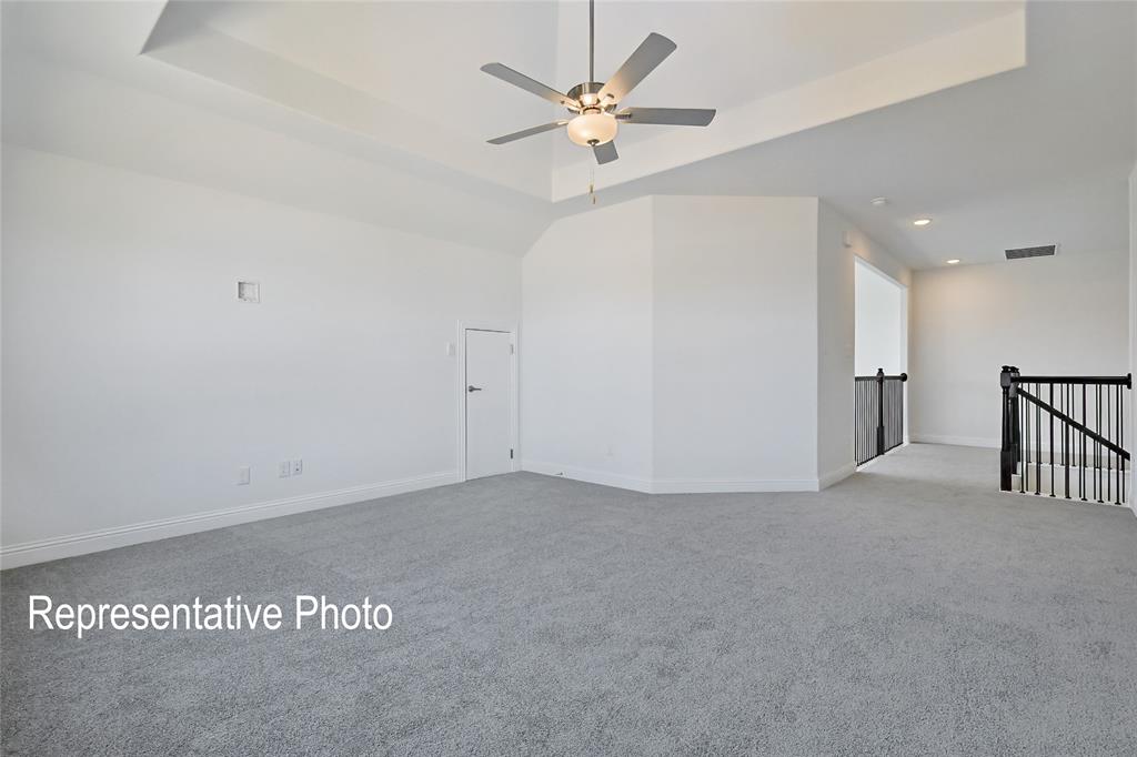 Spacious room featuring light gray carpeting, a tray ceiling, and a ceiling fan with integrated lighting