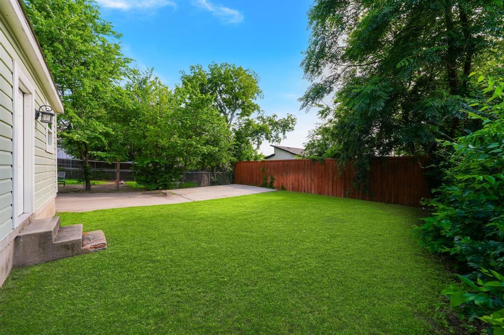 Expansive green lawn with mature trees and a privacy fence