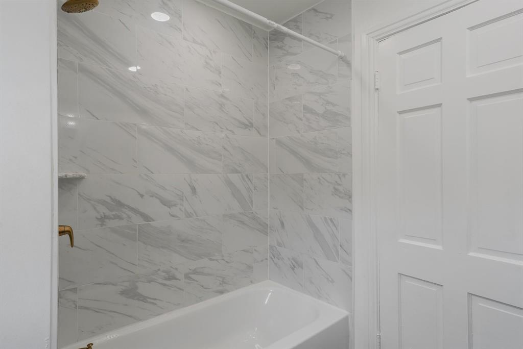 Bathtub with marble-look tile surround, recessed lighting, and gold rainfall shower head