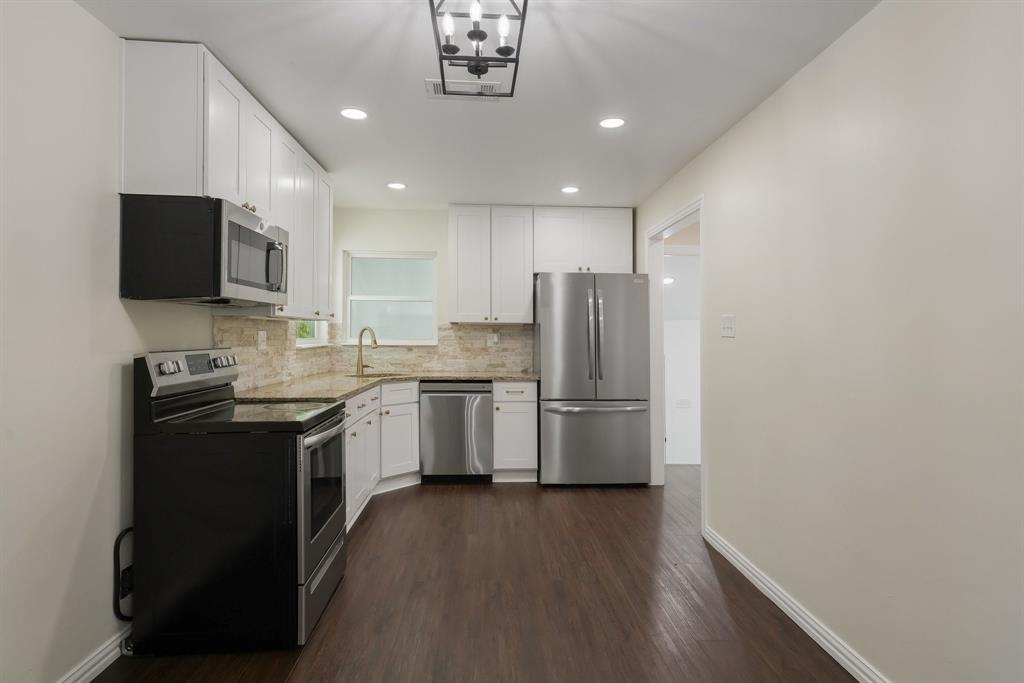 Modern kitchen featuring white cabinetry, stainless steel appliances, granite countertops, gold fixtures.
