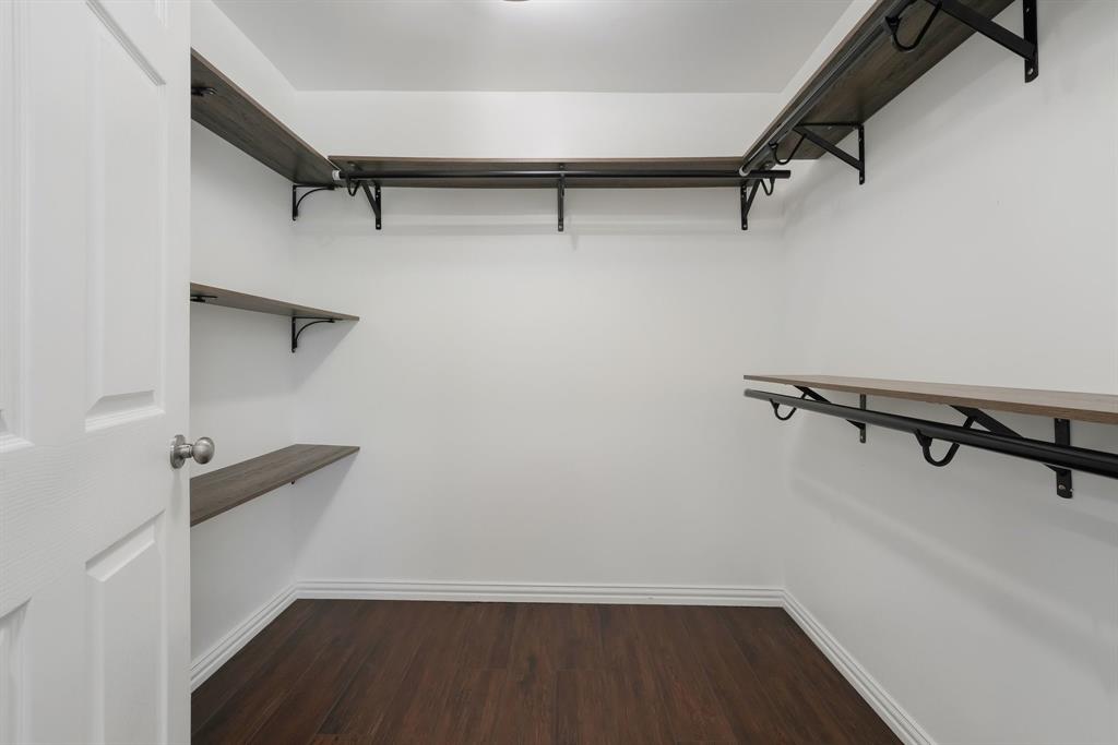 Spacious walk-in closet featuring white walls, and built-in shelving with hanging rods