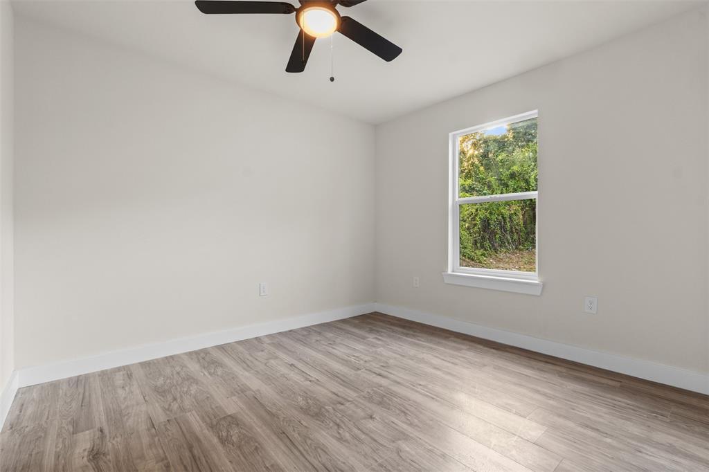 Neutral wall finishes with wood-finish flooring, a ceiling fan with integrated lighting, and a single window with white trim