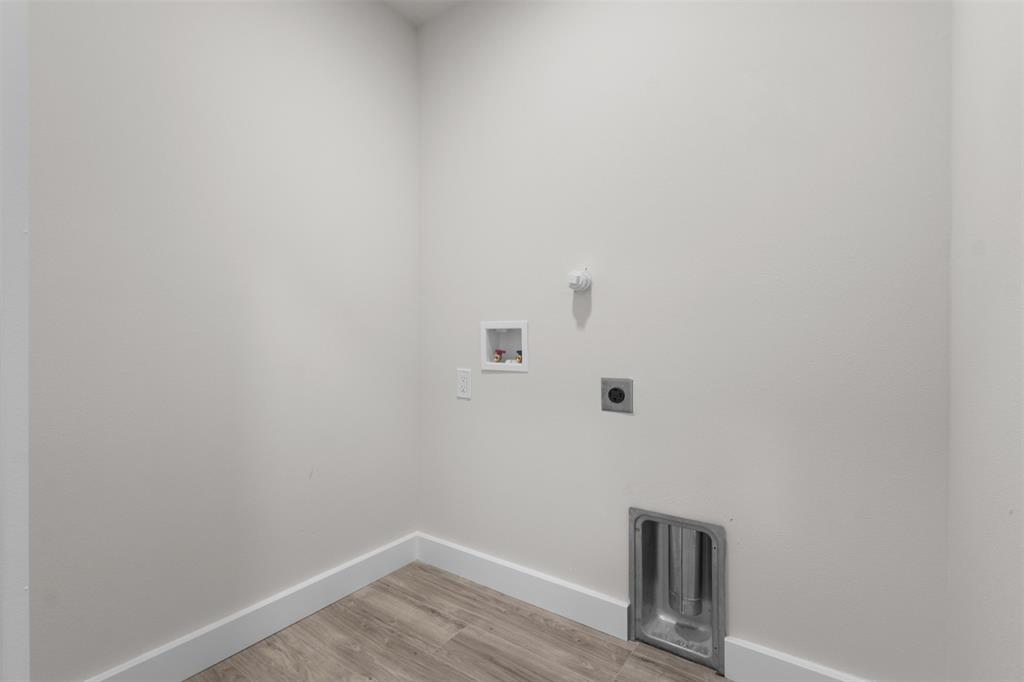Dedicated utility space featuring light-toned walls, wood-finish flooring, and crisp white baseboards