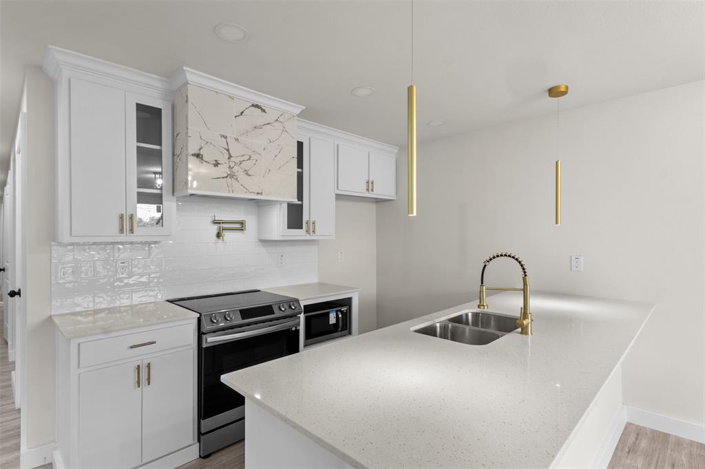 Modern kitchen featuring white cabinetry with gold-tone hardware, a striking marble-patterned range hood, white subway tile backsplash, and light-colored countertops