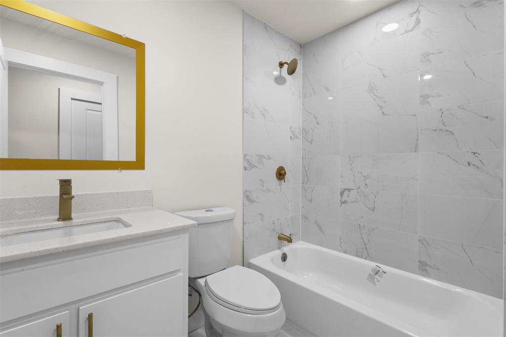 Bathroom featuring a vanity with an integrated sink, a gold-framed mirror, and a toilet
