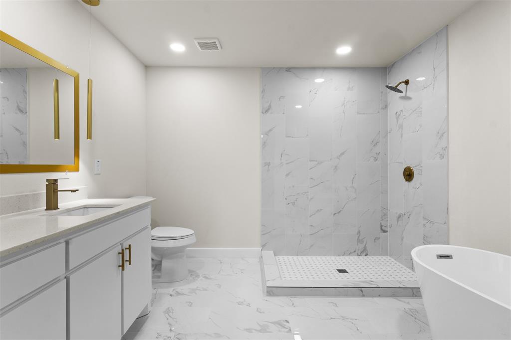 Bathroom featuring a free-standing soaking tub, walk-in shower with large format tile, white vanity with integrated sink, quartz-finish countertop, and gold-finish fixtures