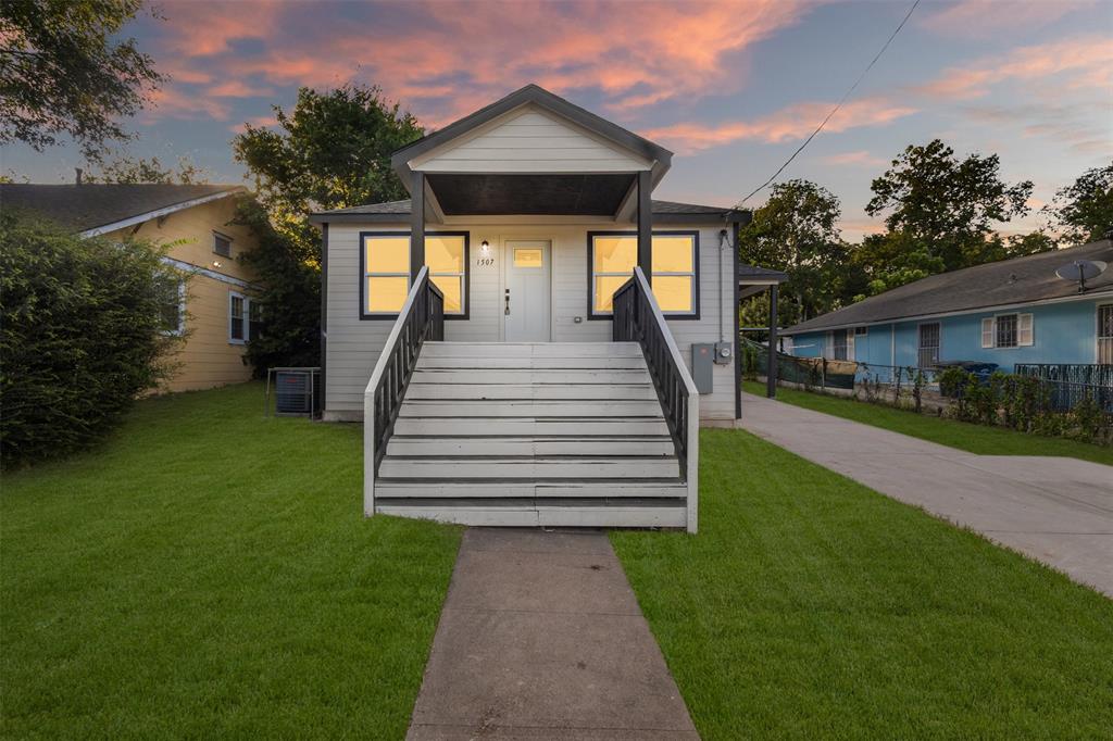 Exterior featuring a central entrance with a covered porch, white siding, dark trim windows, and a manicured lawn Exterior featuring a central entrance with a covered porch, white siding, dark trim windows, and a manicured lawn