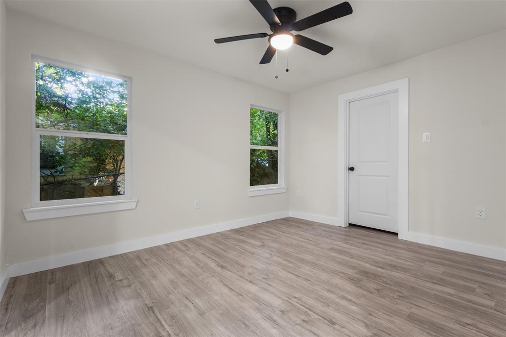 Room featuring two windows, wood-finish flooring, a ceiling fan with light fixture, and a paneled interior door with dark hardware