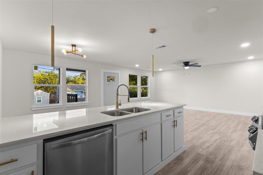 Open-concept kitchen featuring a large island with a double basin sink, light-toned countertops, and contemporary pendant lighting
