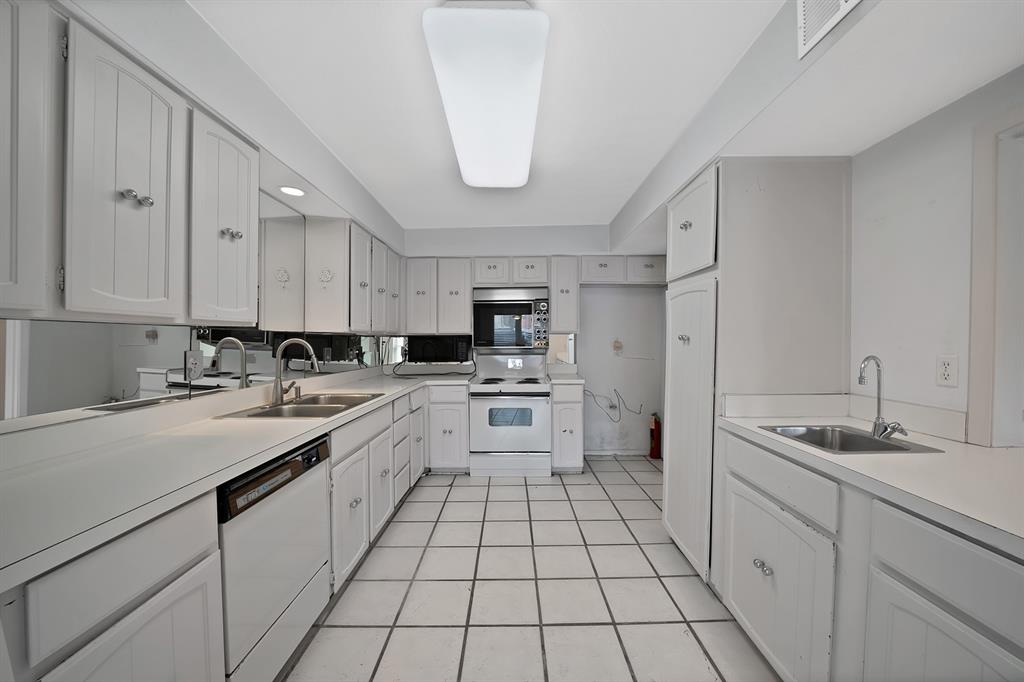 Galley kitchen featuring extensive white cabinetry, white countertops, tile flooring, mirrored backsplash, and a double basin sink