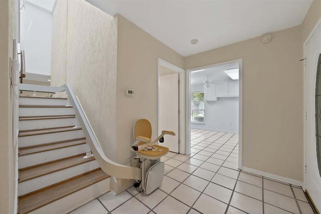 Entry foyer featuring white square tile flooring with contrasting grout, a wood-finish staircase with white risers and railing, an integrated stair lift system, and a front entry door with an oval glass insert