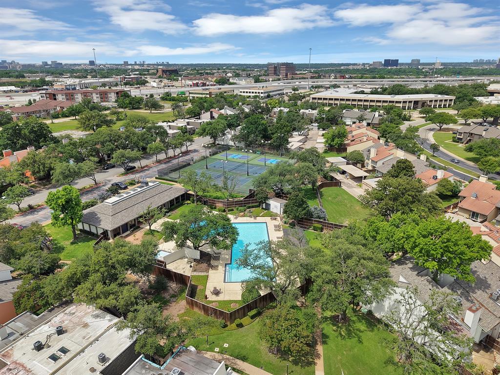Community amenities featuring a central swimming pool with surrounding lounge areas, two tennis courts, and a clubhouse building, all set amidst mature trees and residential structures
