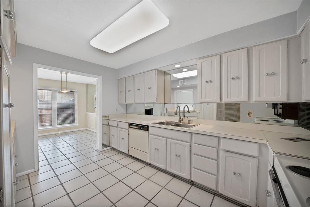 Kitchen featuring white paneled cabinetry, light-toned countertops, a mirrored backsplash, and a double basin sink with a gooseneck faucet