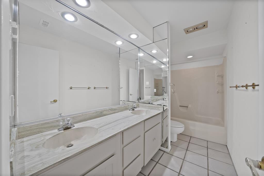 Bathroom featuring a dual-sink vanity with a stone countertop, white cabinetry, and an integrated mirror with overhead lighting