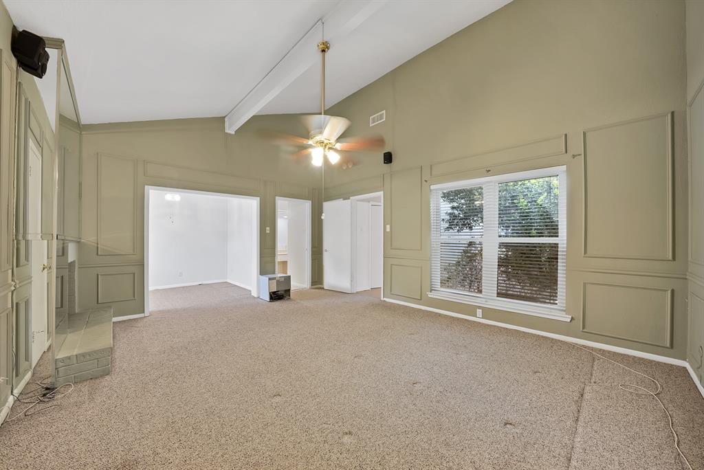 Spacious interior room featuring vaulted ceilings with exposed beams, wainscoting paneling, and an overhead ceiling fan with integrated lighting
