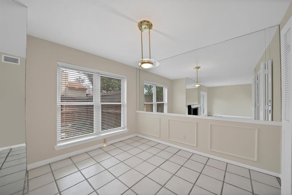 Dining area featuring large window with blinds, overhead lighting fixture, tiled flooring, and a mirrored wall panel