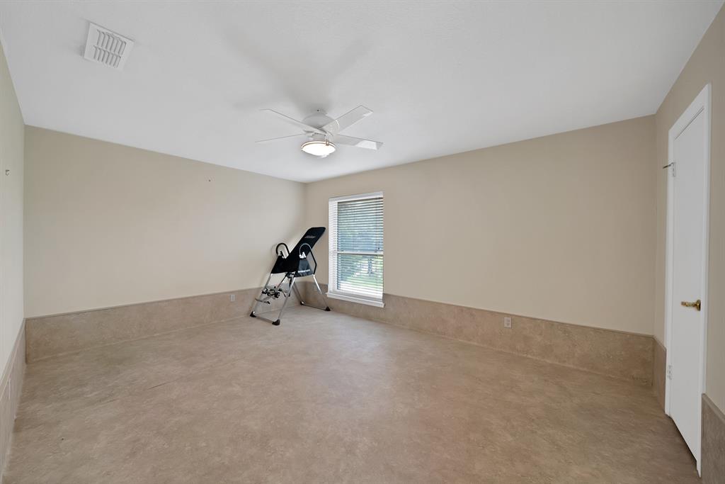 Spacious room featuring neutral-toned walls, a ceiling fan with integrated lighting, a window with blinds, and durable flooring