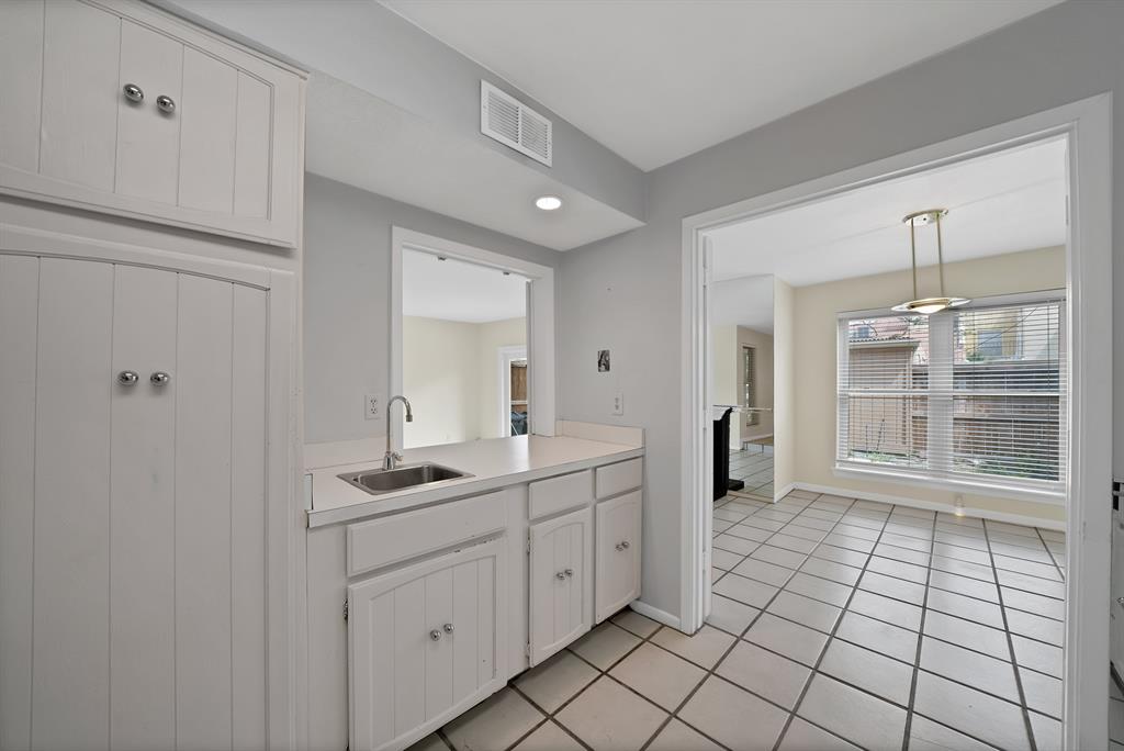 Kitchenette featuring a stainless steel sink with a gooseneck faucet, white cabinetry, and light-toned countertops