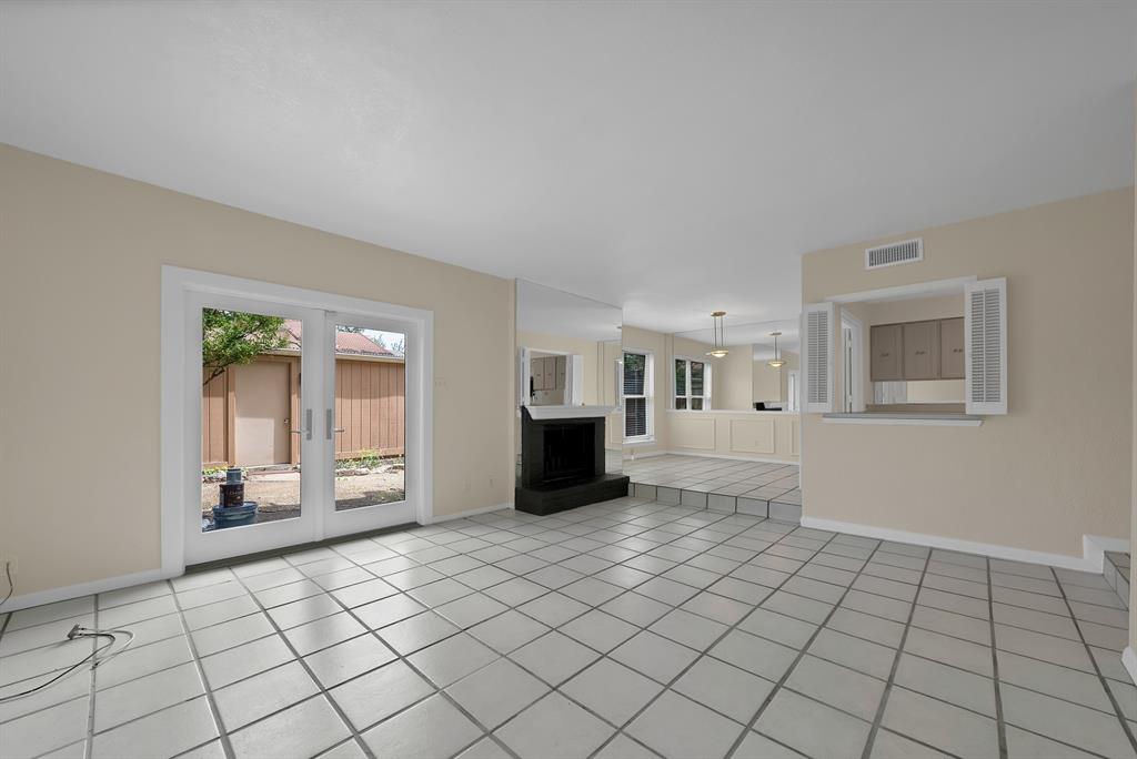 Spacious interior featuring light-colored tile flooring, a black hearth and fireplace, and white-framed glass French doors
