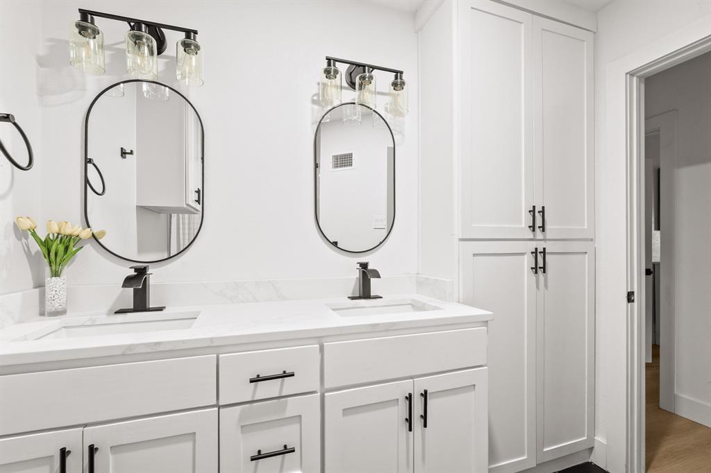 Dual vanity with undermount sinks, quartz countertops, black hardware, oval mirrors, and white shaker-style cabinetry, complemented by a tall built-in storage cabinet