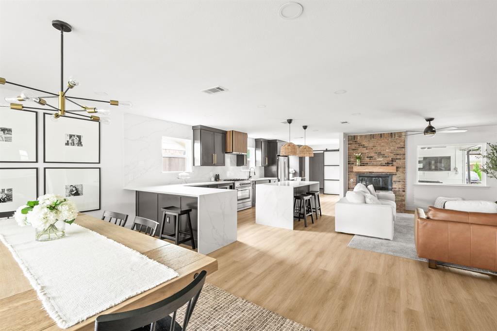Open-concept living area featuring wood-finish flooring, a brick fireplace with a wood mantle, and recessed lighting Open-concept living area featuring wood-finish flooring, a brick fireplace with a wood mantle, and recessed lighting