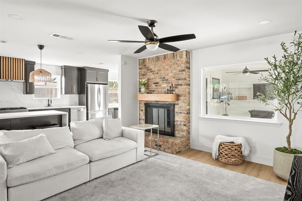 Open-concept living space with a brick fireplace, wood-finish mantel, and a ceiling fan Open-concept living space with a brick fireplace, wood-finish mantel, and a ceiling fan