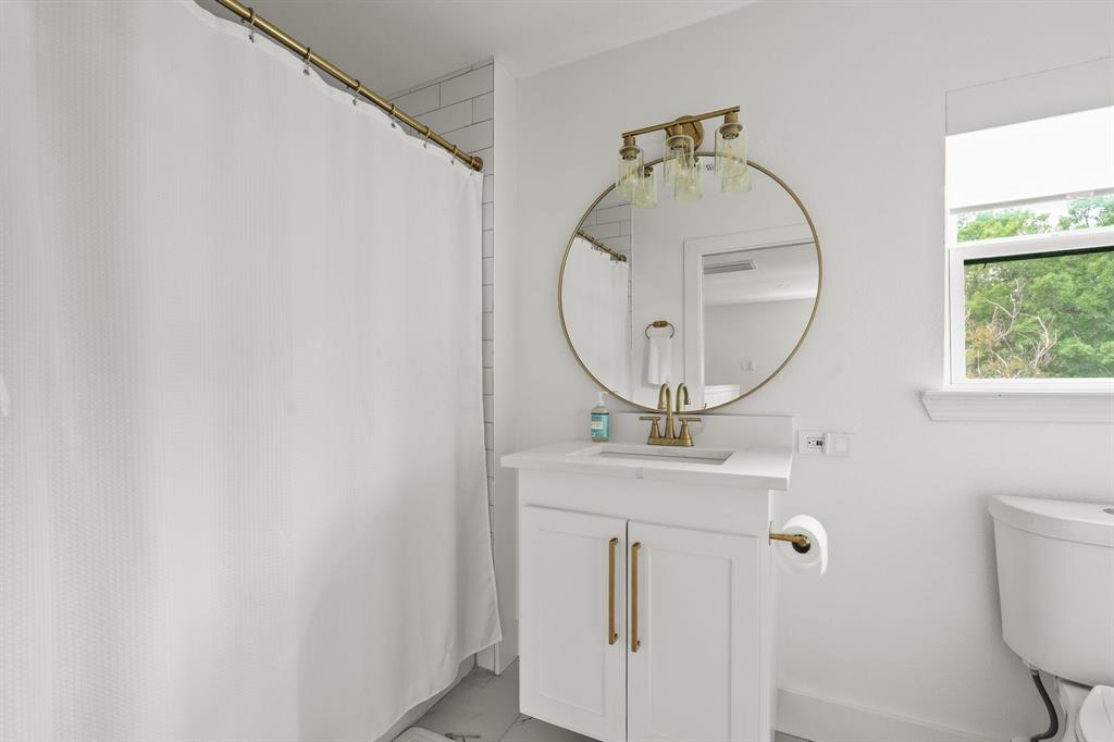 Bathroom featuring a white vanity with gold-finish hardware, a circular gold-framed mirror, and a three-light vanity fixture