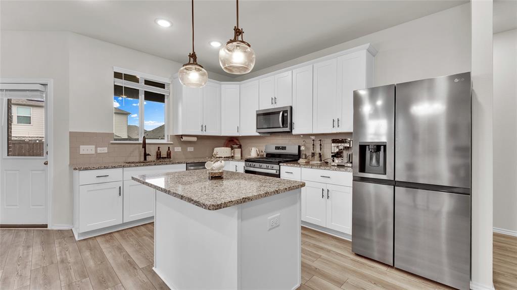 Modern kitchen featuring an island with granite countertops, white cabinetry, stainless steel appliances, wood-finish flooring, and pendant lighting