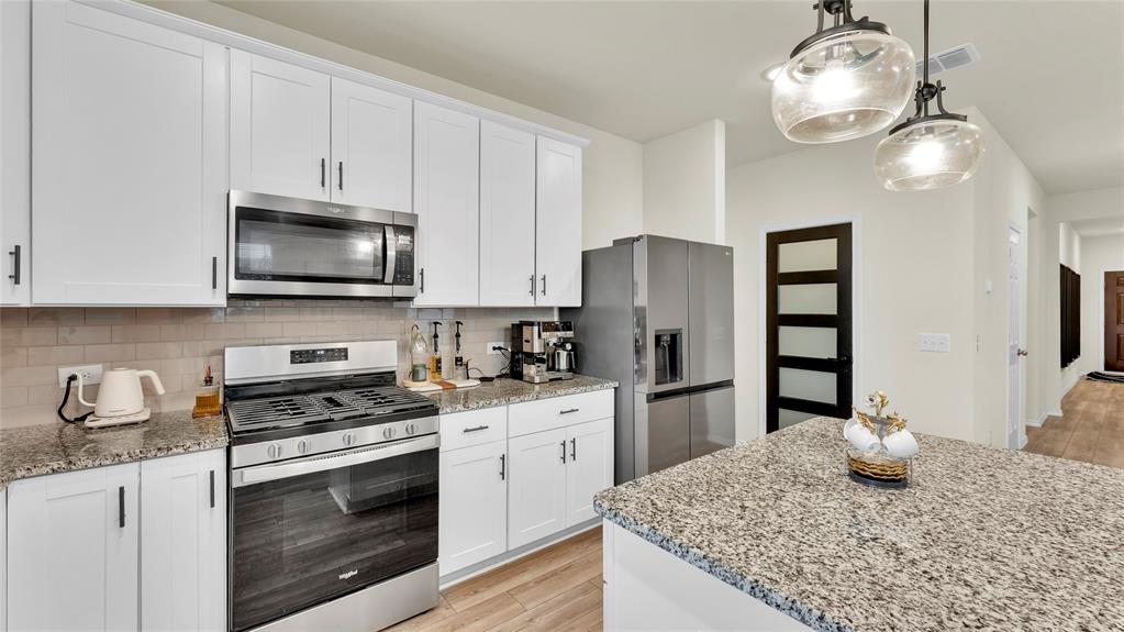 Modern kitchen featuring white shaker cabinetry, stainless steel appliances, speckled stone countertops, and a subway tile backsplash