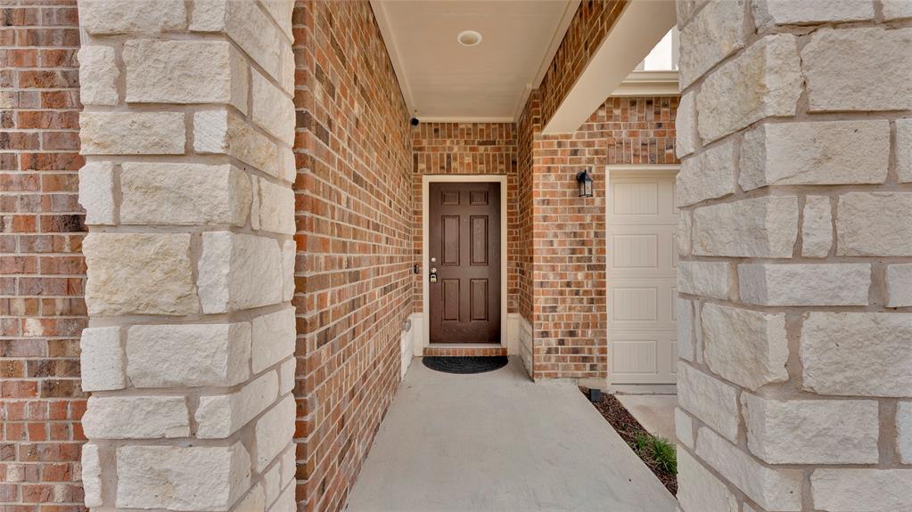 Exterior facade featuring a brown paneled entry door, light brick, stacked stone accents, and a panel-style garage door