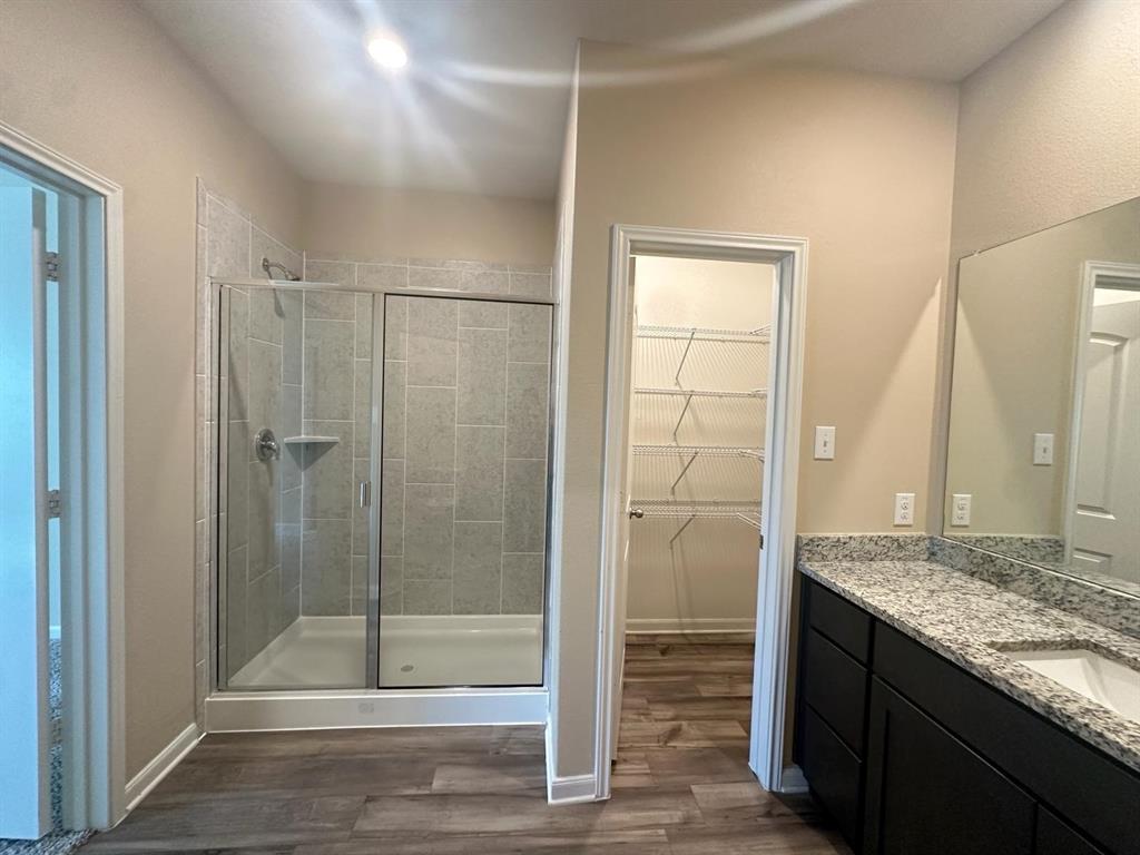 Bathroom featuring a glass-enclosed shower with tile surround, a spacious vanity with a speckled countertop and integrated sink, dark wood-finish cabinetry, and wood-finish flooring