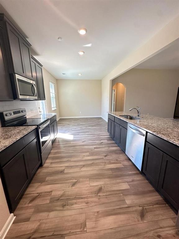 Kitchen featuring dark wood cabinetry, granite-style countertops, stainless steel appliances, and wood-finish flooring