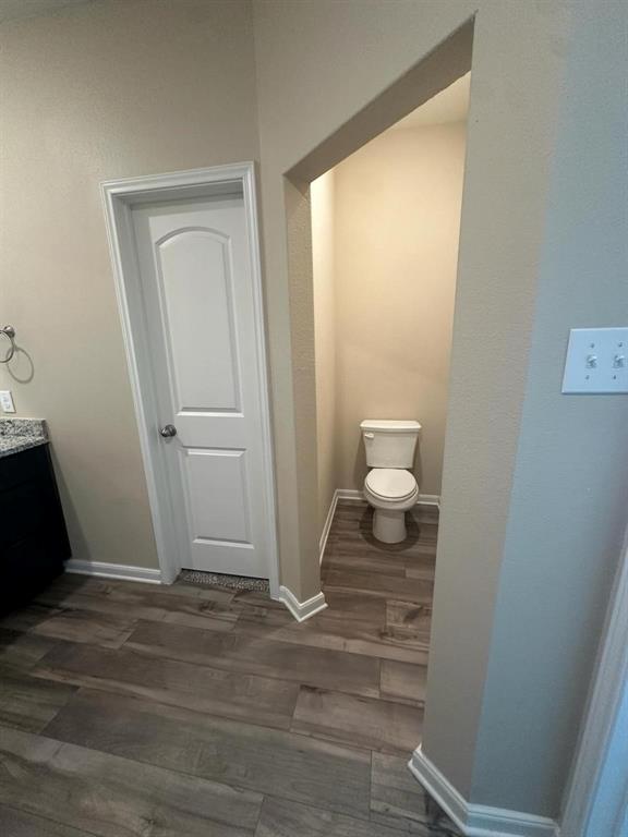 Dedicated water closet featuring wood-finish flooring, neutral wall tones, and crisp white baseboards