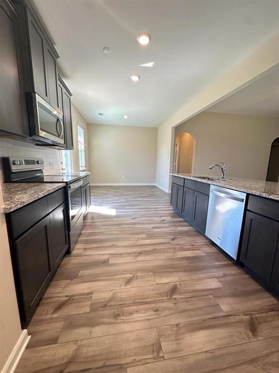 Modern kitchen featuring dark cabinetry, stainless steel appliances, speckled stone countertops, and wood-finish flooring