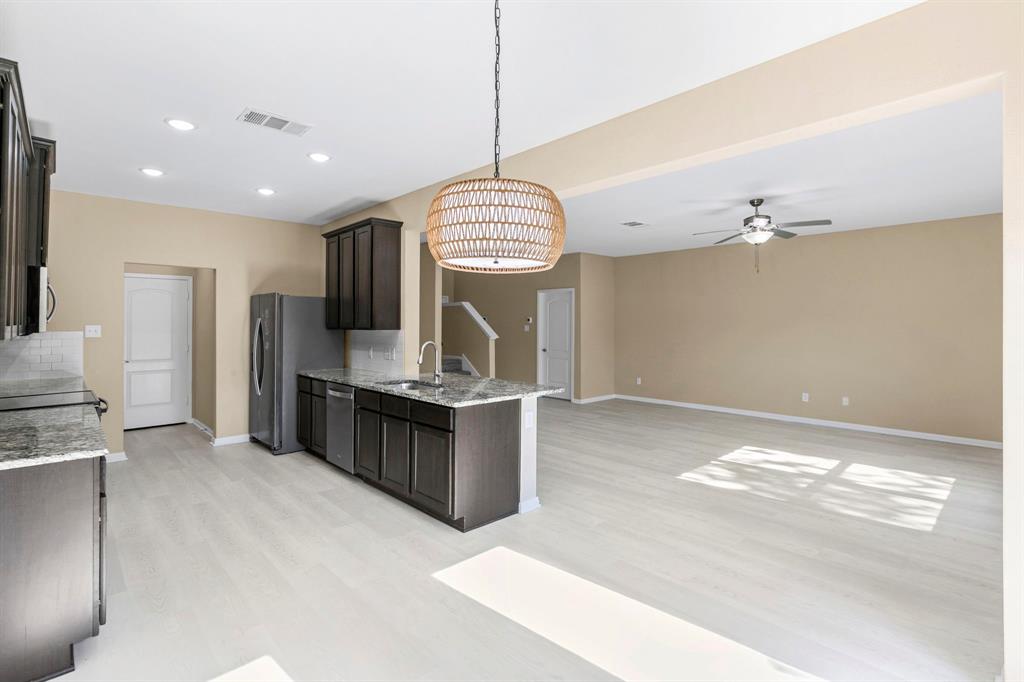 Open-concept kitchen featuring dark wood cabinetry, light wood-finish flooring, and a kitchen island with sink Open-concept kitchen featuring dark wood cabinetry, light wood-finish flooring, and a kitchen island with sink