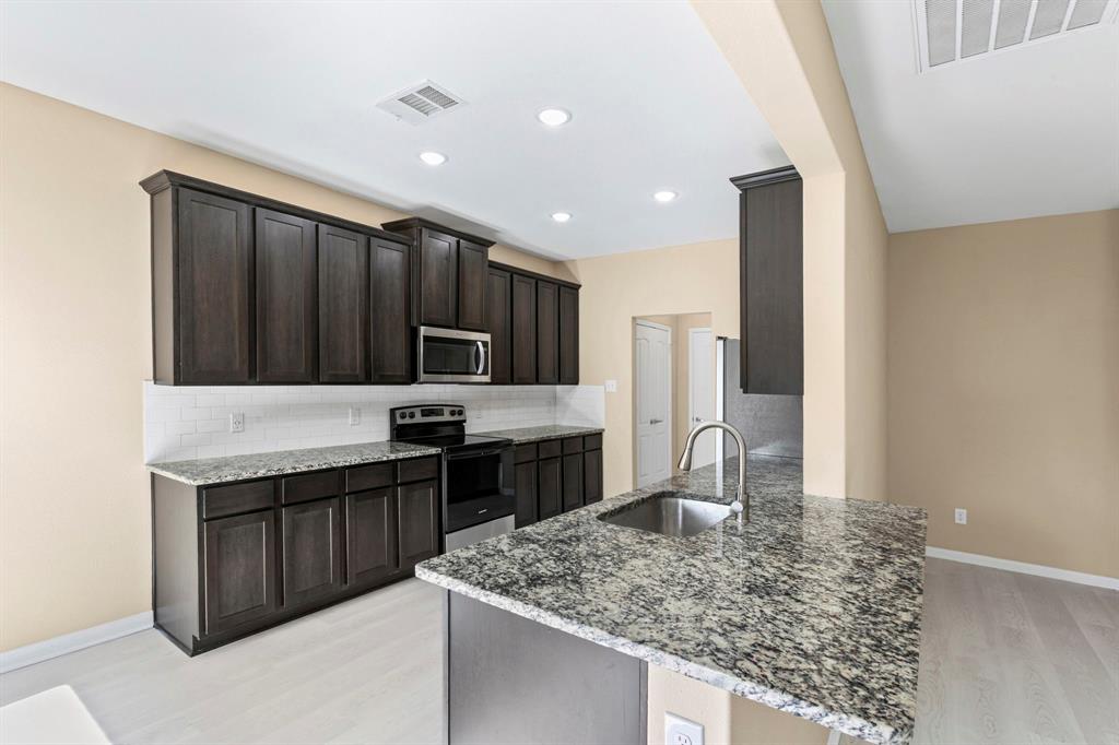 Kitchen featuring dark wood cabinetry, light-colored granite countertops, and a subway tile backsplash Kitchen featuring dark wood cabinetry, light-colored granite countertops, and a subway tile backsplash