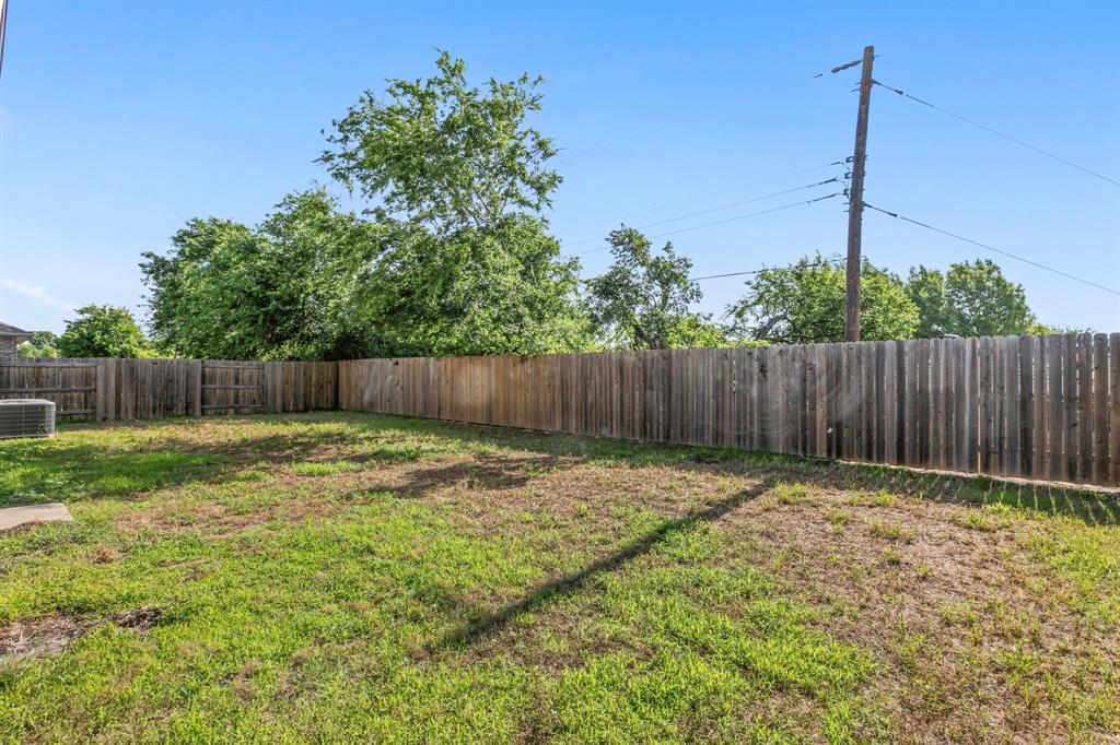 Expansive backyard space featuring a wooden privacy fence, mature trees, and a ground-mounted HVAC unit