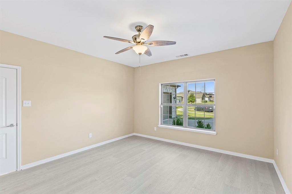 Spacious room featuring light wood-finish flooring, a ceiling fan with integrated lighting, and a white interior door