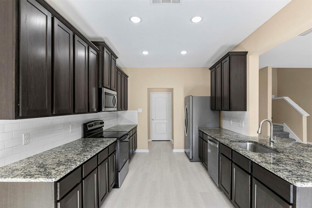 Galley kitchen featuring dark wood-finish cabinetry, granite-style countertops, stainless steel appliances, and white subway tile backsplash Galley kitchen featuring dark wood-finish cabinetry, granite-style countertops, stainless steel appliances, and white subway tile backsplash